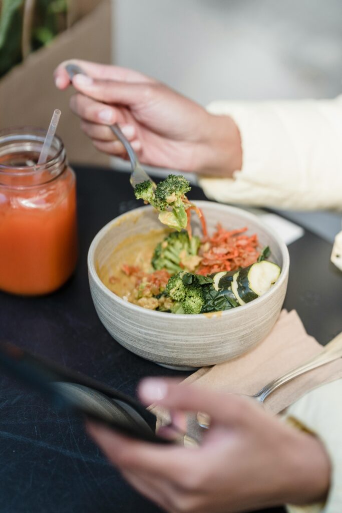 From above of crop unrecognizable person with cellphone at street cafeteria table with yummy vegetable salad and smoothie